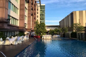A hotel pool area with tables and chairs set up for an event, surrounded by buildings with balconies and a clear sky.
