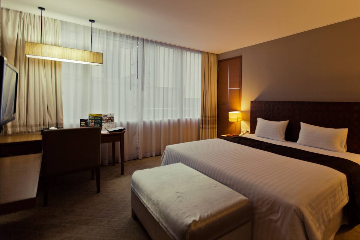 Habitación de hotel con una cama grande, un escritorio, una silla y una mesita de noche con lámpara.