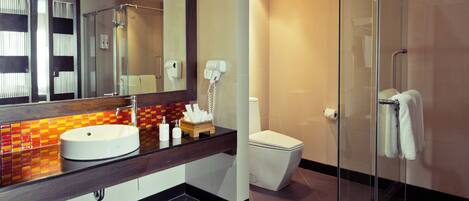 Un baño moderno con cabina de ducha de vidrio, inodoro blanco y tocador con espejo y lavamanos.