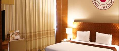 Una suite junior tipo B en Suntee Tower, con una cama grande, una mesita de noche, una lámpara y un ventanal con cortinas.