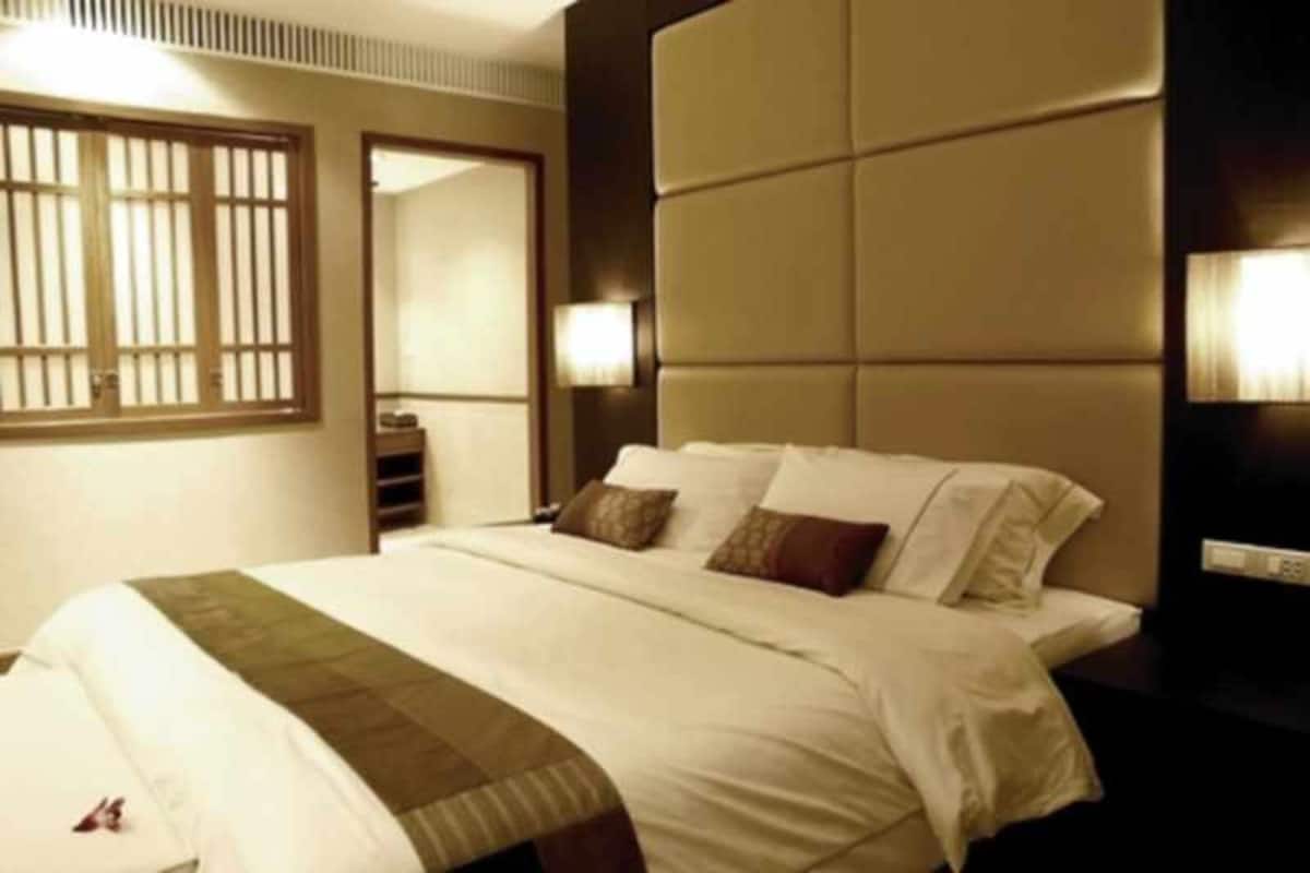 Habitación de hotel con una cama grande, cabecera con diseño acolchado, mesita de noche con lámpara y ventana con persianas verticales.