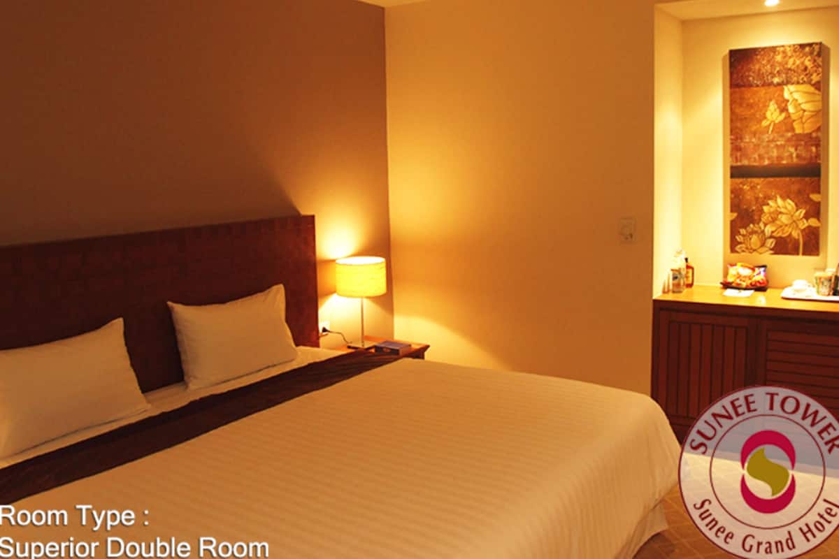 Una habitación doble superior en Sunnee Tower, con una cama grande con ropa blanca, un cabecero de madera, una lámpara de noche y una mesita con hervidor y aperitivos.