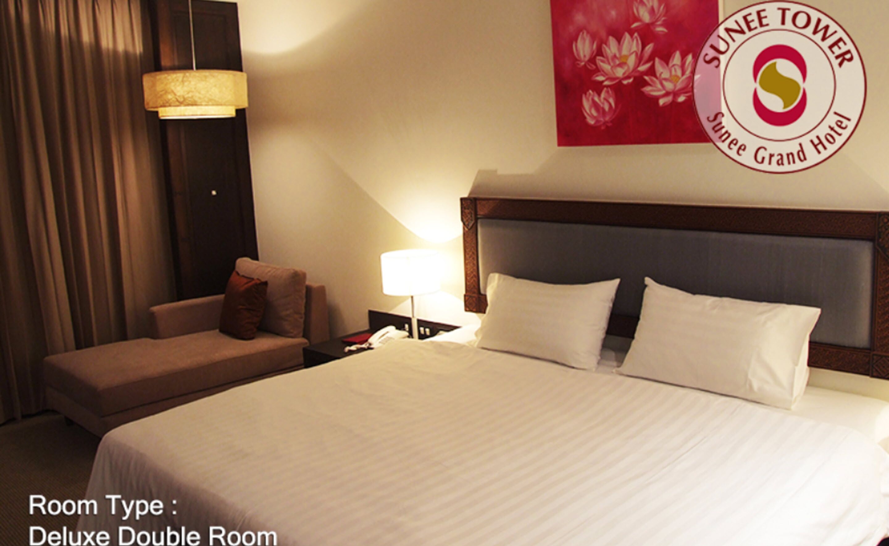 A Deluxe Double Room with a bed, bedside table, lamp, and a sofa.