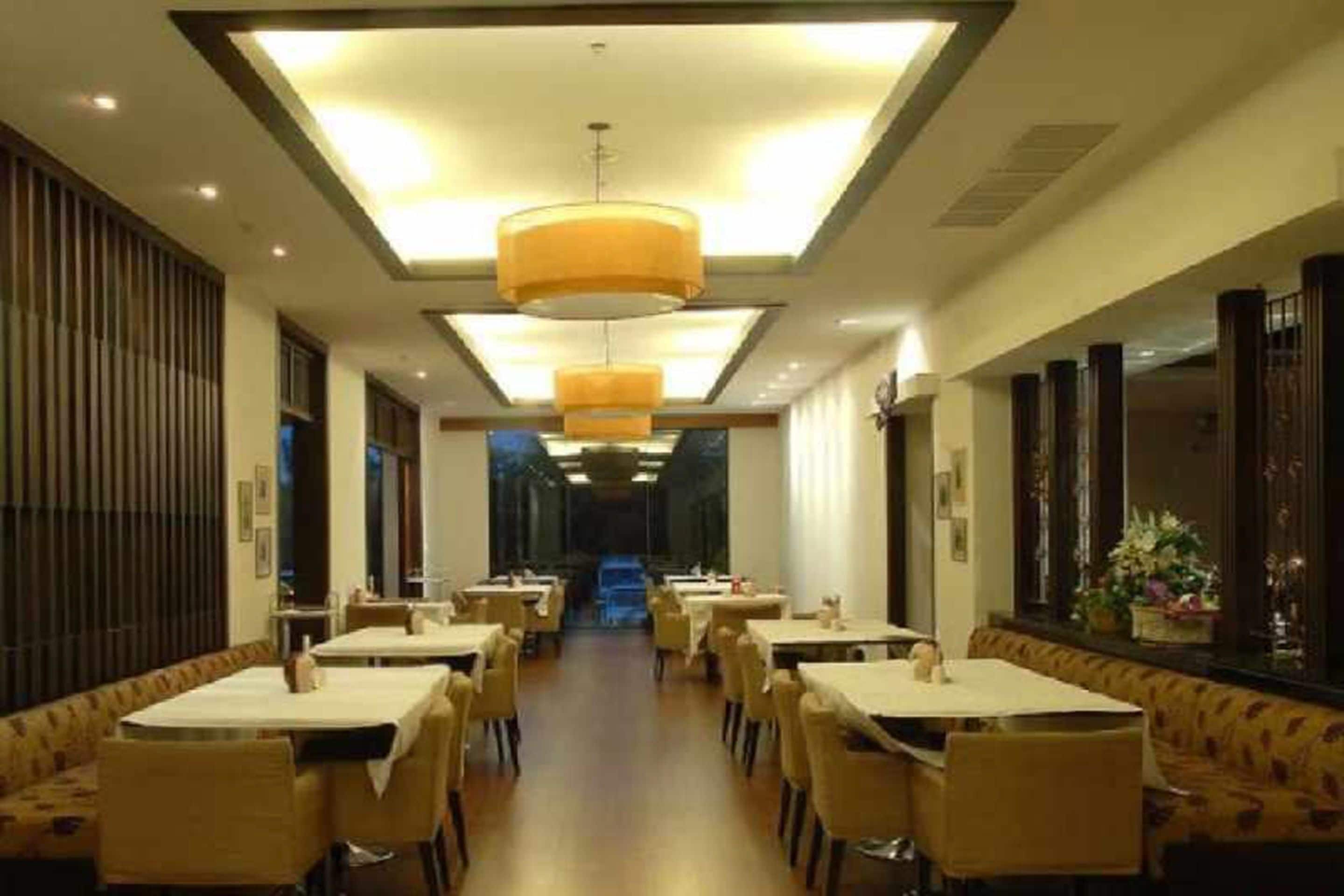 A restaurant with multiple tables and chairs, a central walkway, and hanging pendant lights.