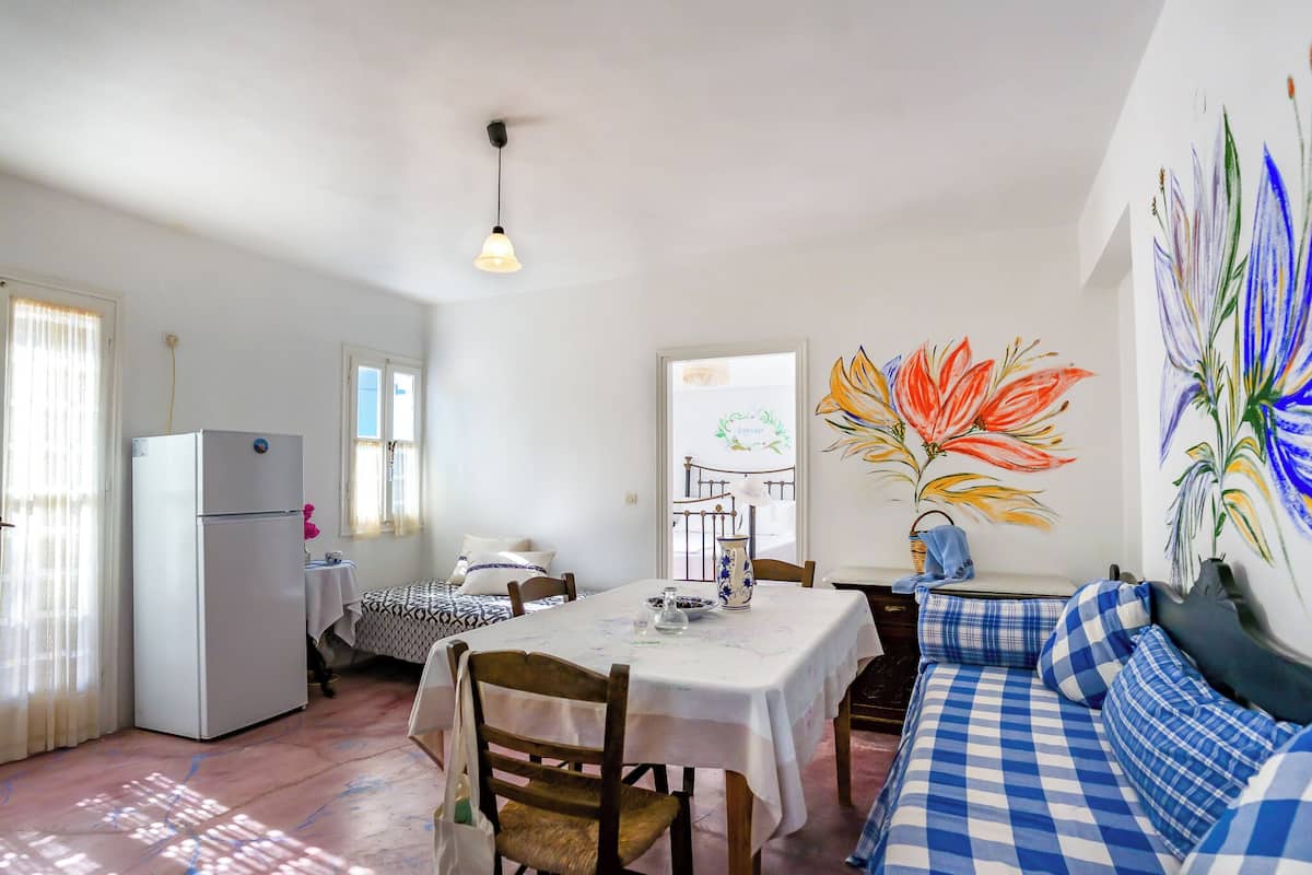Un comedor con una mesa preparada para dos personas, un refrigerador y un sofá con cojines a cuadros.