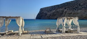 A beach with two white canopied seating areas, a rocky shoreline, and a sailboat in the distance.