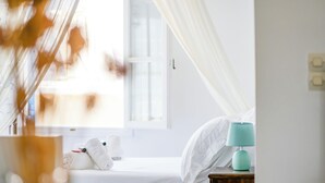 Un dormitorio con cama, ropa de cama blanca, una lámpara verde azulada y una ventana con cortinas.