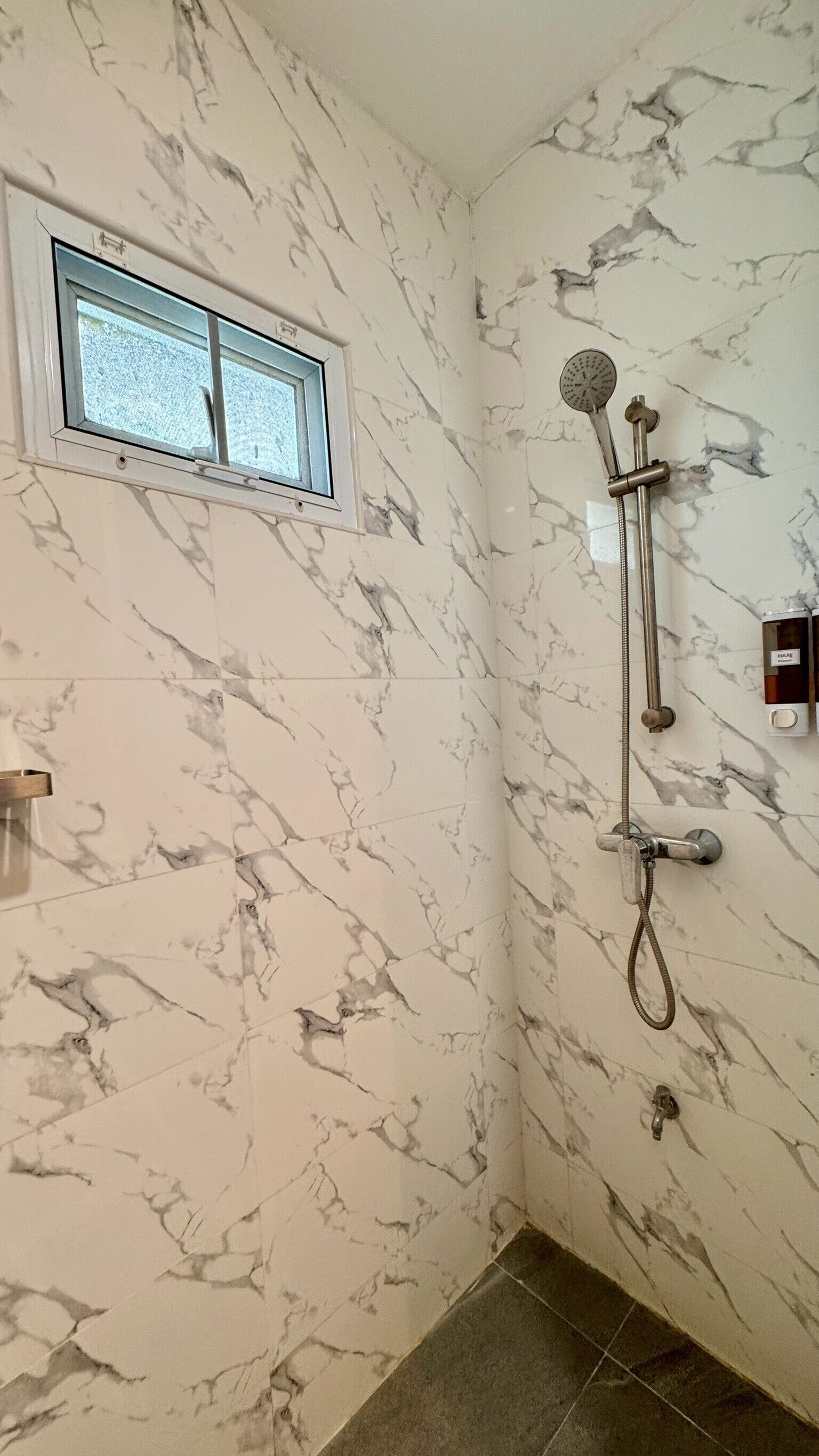 Baño con paredes de mármol, ventana, ducha e inodoro.