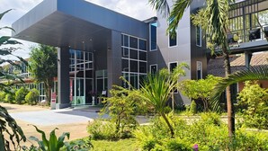 A modern building with large windows and a well-maintained garden with various plants and flowers. - Baan Suan Khunta Golf Resort (Warin Chamrap)