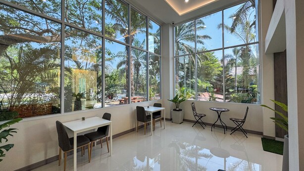 A spacious room with large windows, a white table, and chairs, and a small round table with chairs. - Baan Suan Khunta Golf Resort (Warin Chamrap)
