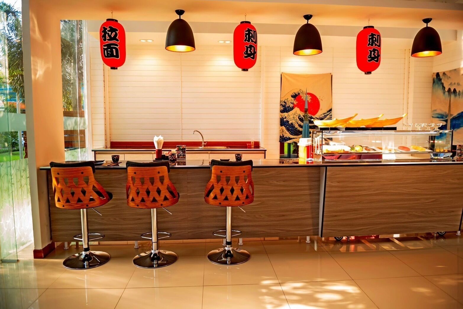 A restaurant with a sushi bar, wooden bar stools, and red lanterns.