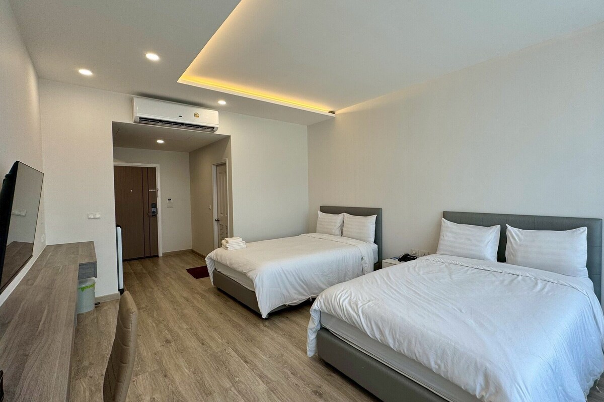 A hotel room with two beds, a TV, and an air conditioning unit.
