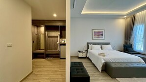 A modern hotel room with a wooden floor, a bed with a grey headboard, a bedside table, a nightstand, a window with curtains, and a painting on the wall. - Baan Suan Khunta Golf Resort (Warin Chamrap)