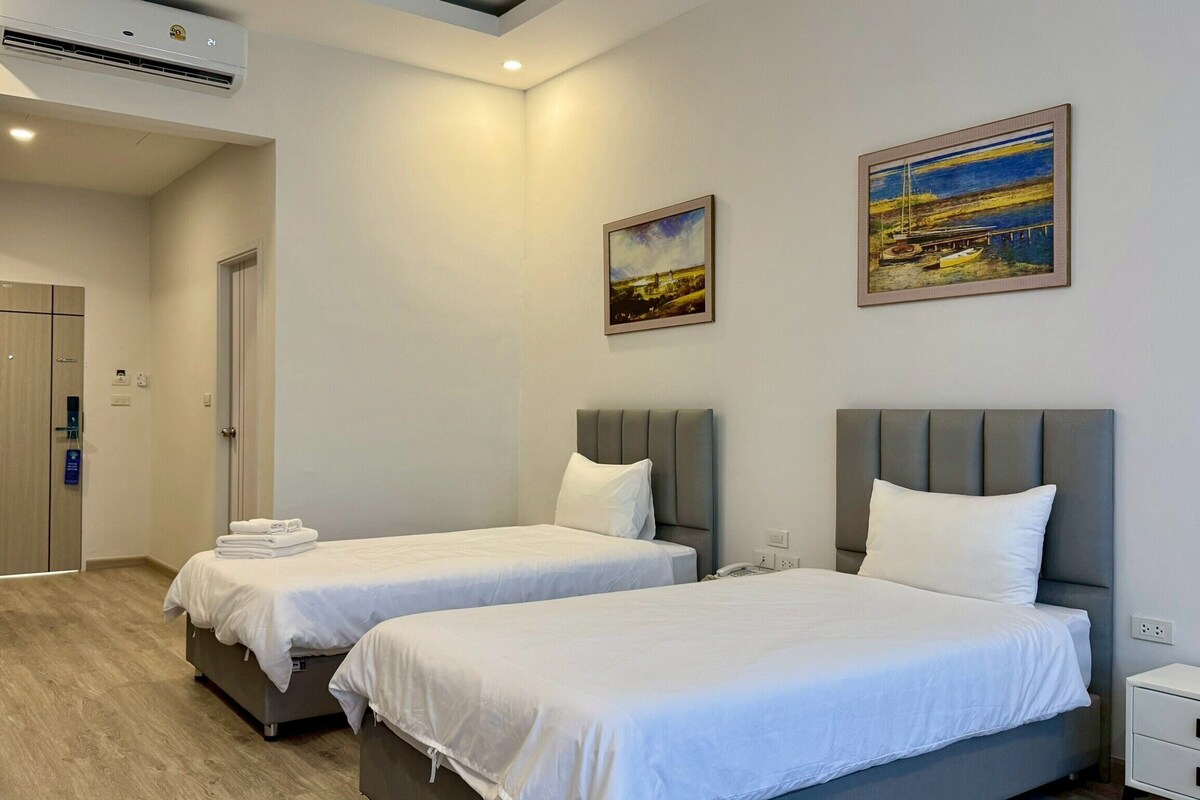 A hotel room with two single beds, a desk, a chair, and a painting on the wall.