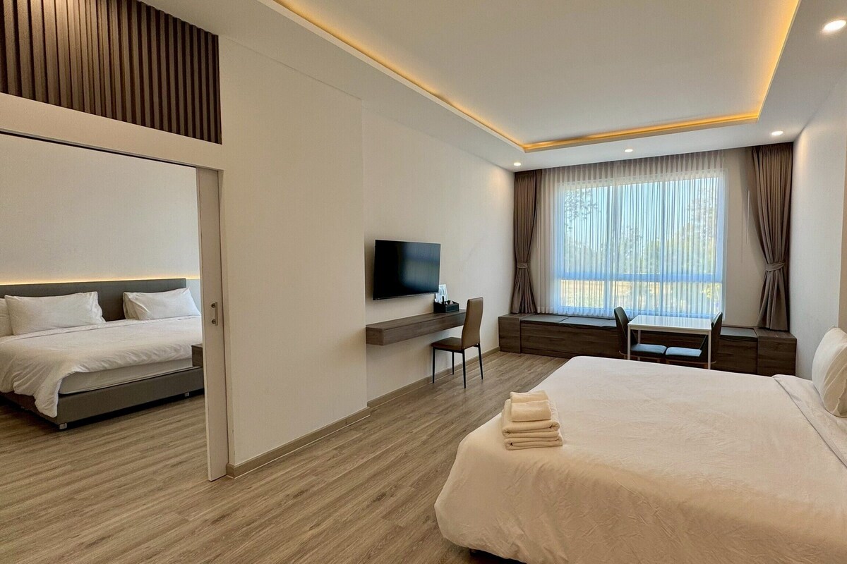 Ein modernes Hotelzimmer mit einem großen Bett, einem Schreibtisch, einem Fernseher und einem Fenster mit Vorhängen.
