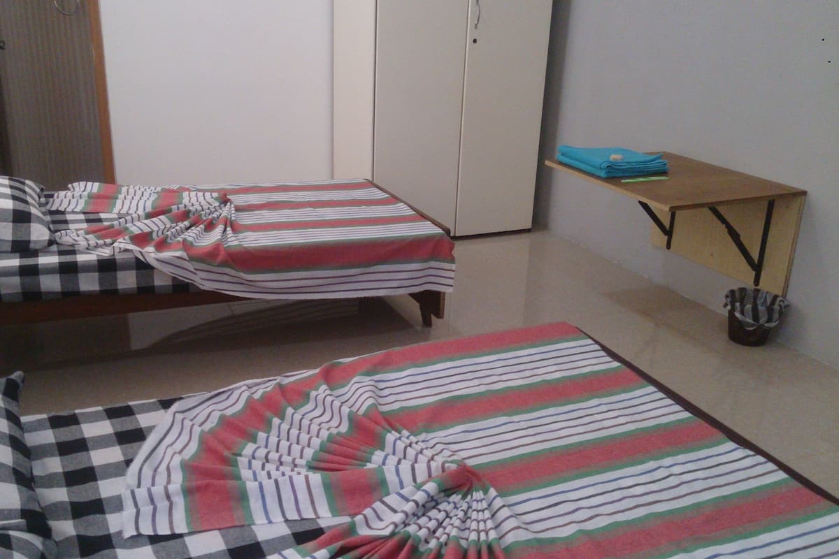 Two single beds with striped bedding in a room with a wooden table and a trash bin.