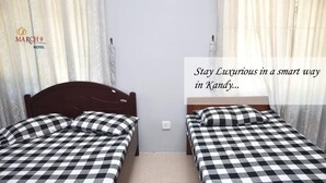 Ett hotellrum med två sängar, rutigt sänglinne, en randig matta och gardiner.