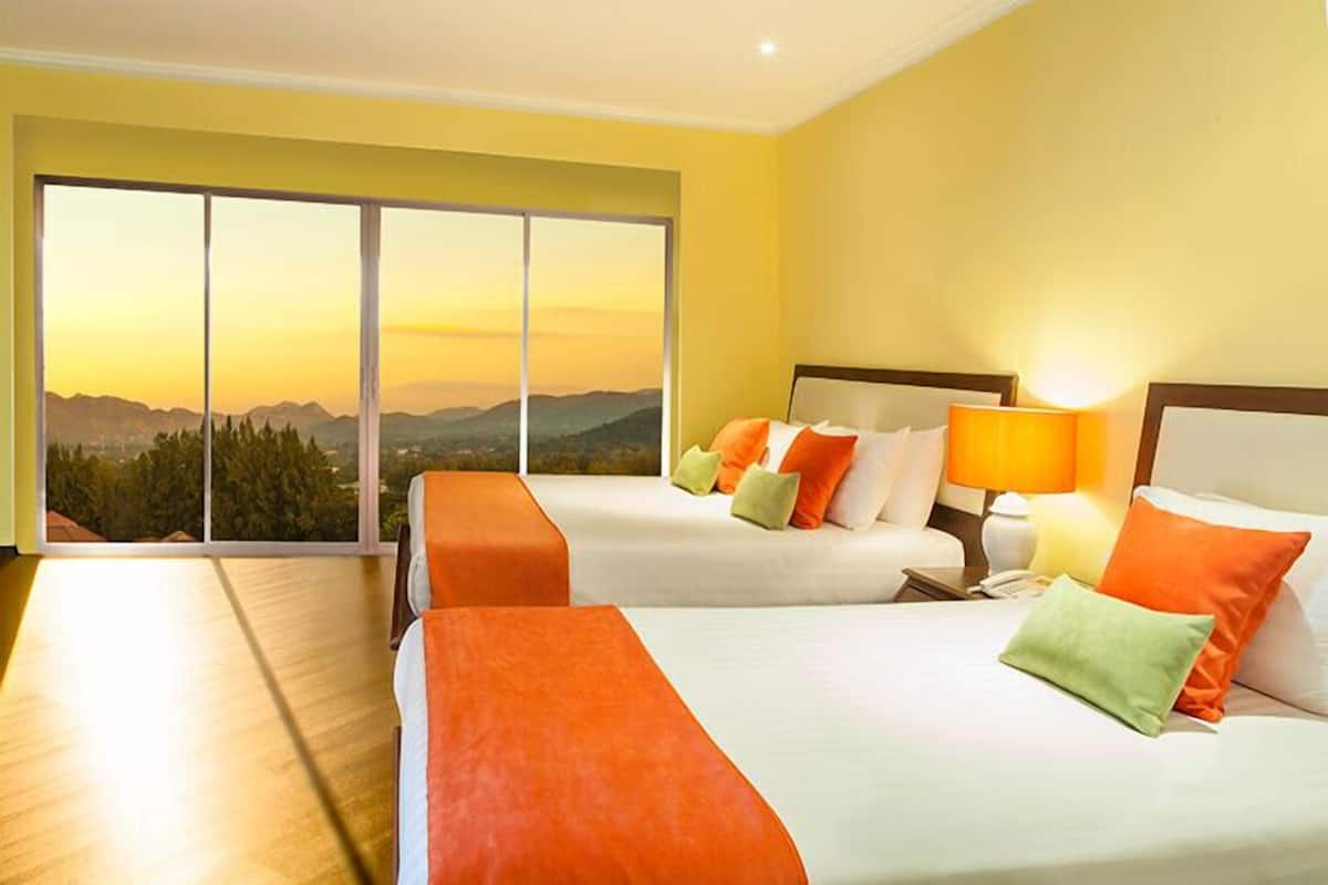 Habitación de hotel con dos camas, un ventanal con vistas a la montaña y suelo de madera.