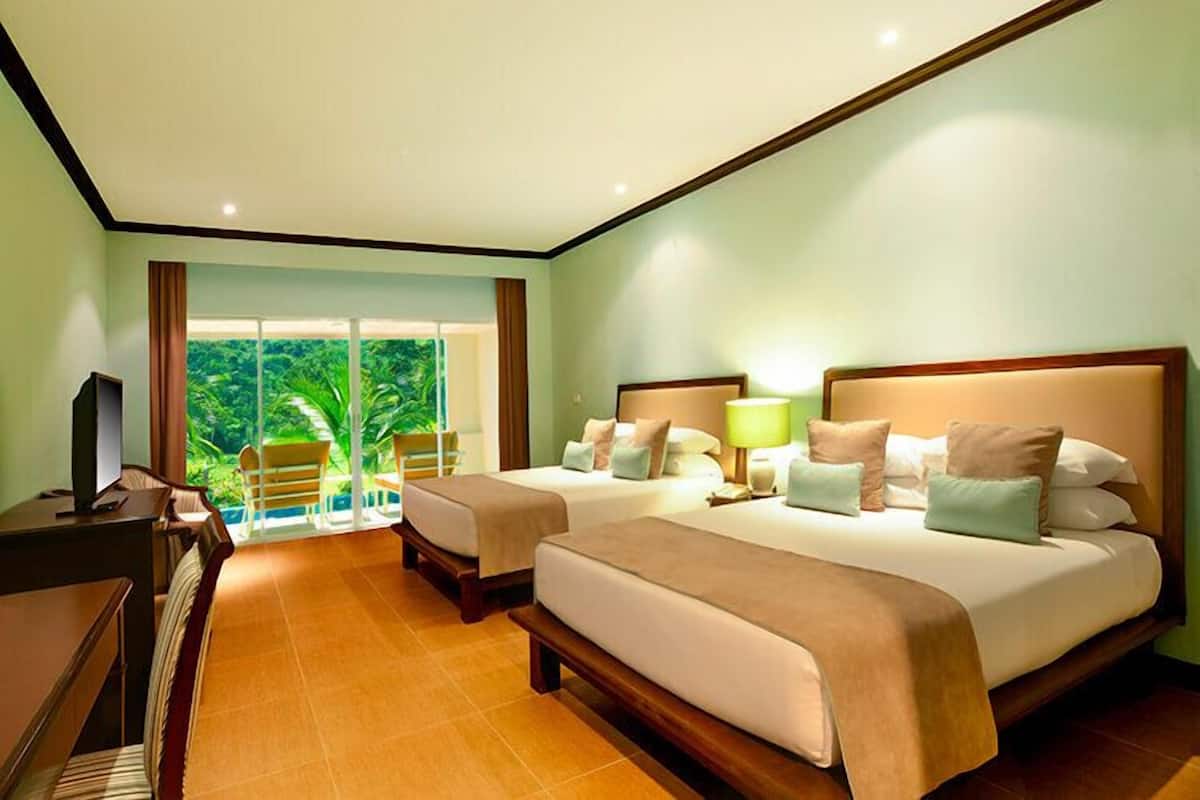 Una habitación de hotel con dos camas, un escritorio y vistas a un jardín exuberante.