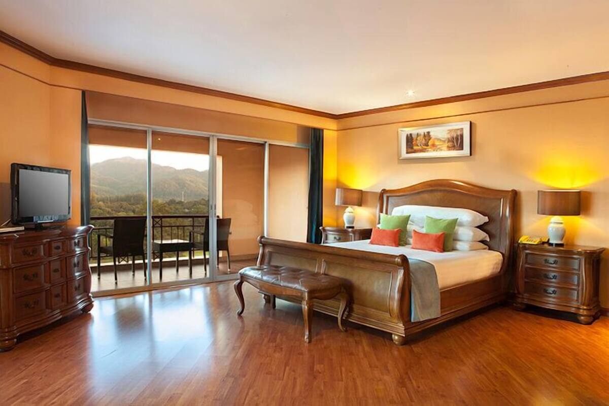 Un dormitorio amplio con una cama grande, un banco de madera, un televisor y un balcón con vistas a la montaña.