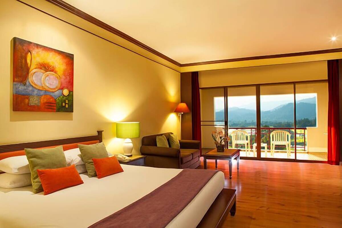 Un cuarto de hotel con una cama grande, un cuadro en la pared, un balcón con vistas a las montañas y una mesa con sillas.
