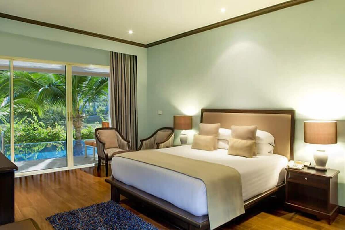 Un dormitorio con una cama grande, una mesita de noche, una lámpara y vistas a una piscina a través de una puerta corrediza.