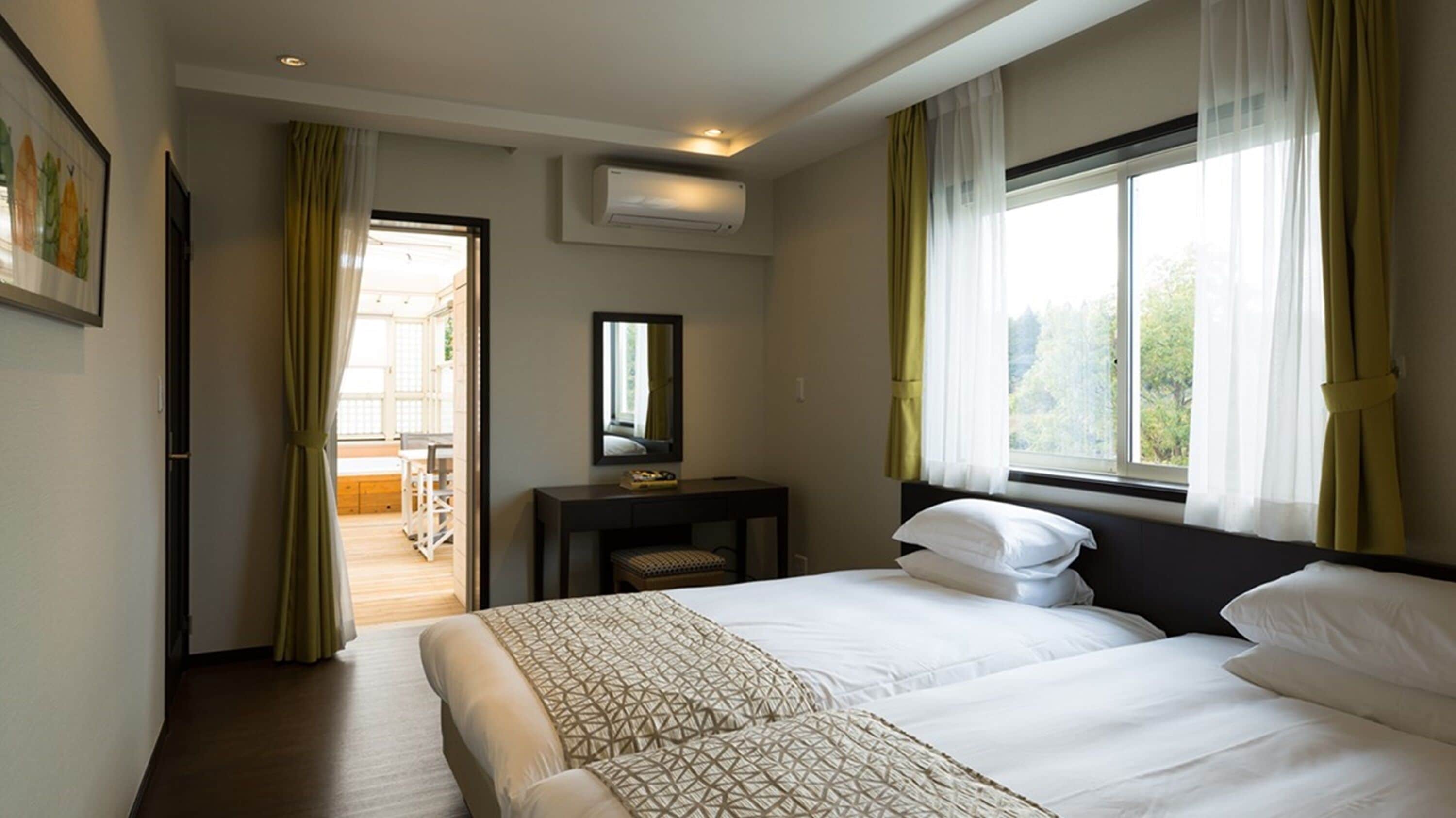 Ein Hotelzimmer mit zwei Betten, einem Schreibtisch, einem Stuhl, einem Spiegel und einem Fenster mit Vorhängen.