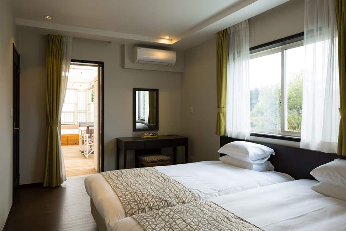Ein Hotelzimmer mit zwei Betten, einem Schreibtisch, einem Stuhl, einem Spiegel und einem Fenster mit Vorhängen.