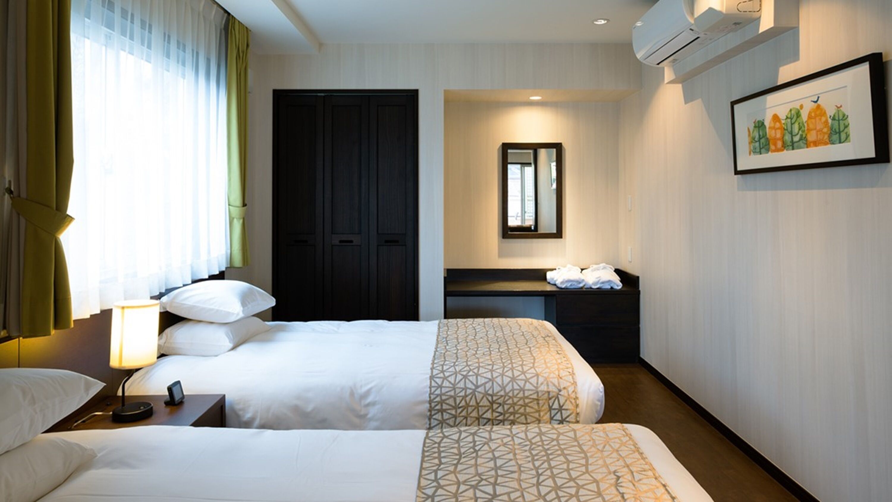Ein Hotelzimmer mit zwei Betten, einem Schreibtisch, einem Spiegel und einem gerahmten Bild an der Wand.