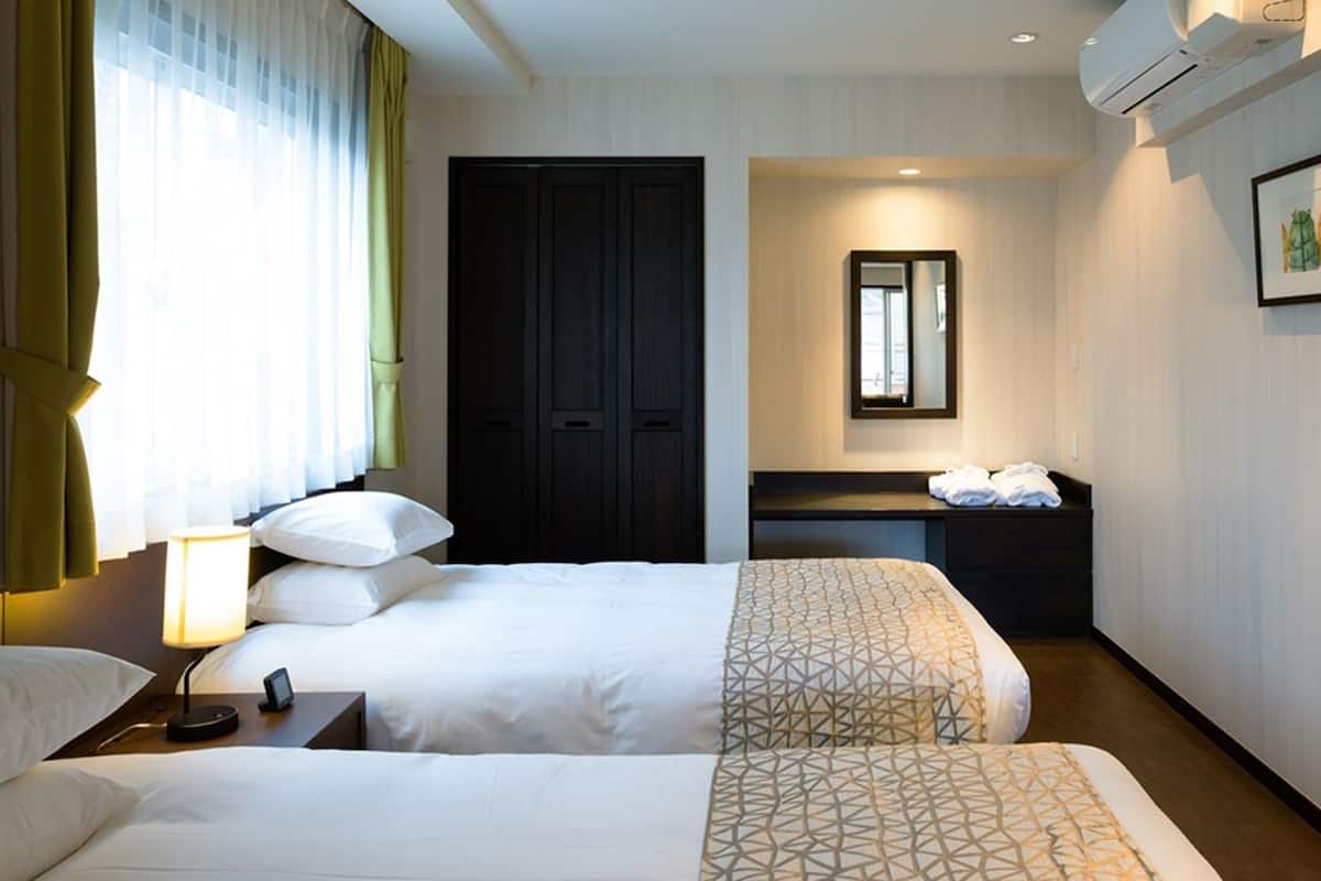 Ein Hotelzimmer mit zwei Betten, einem Schreibtisch, einem Spiegel und einem gerahmten Bild an der Wand.
