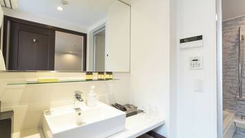 Un baño moderno con un espejo grande, lavabo blanco y estante de vidrio con artículos de aseo.