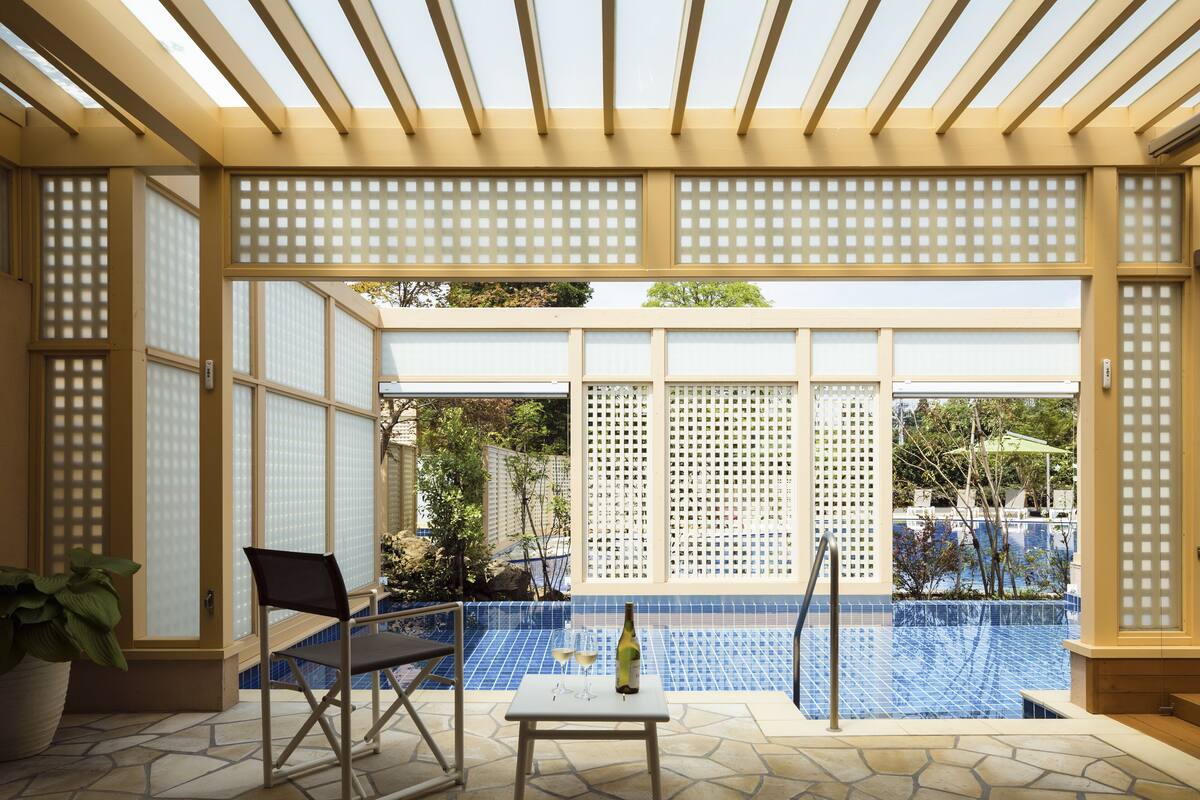 A covered outdoor area with a pool, a table with a bottle and glasses, and a chair.