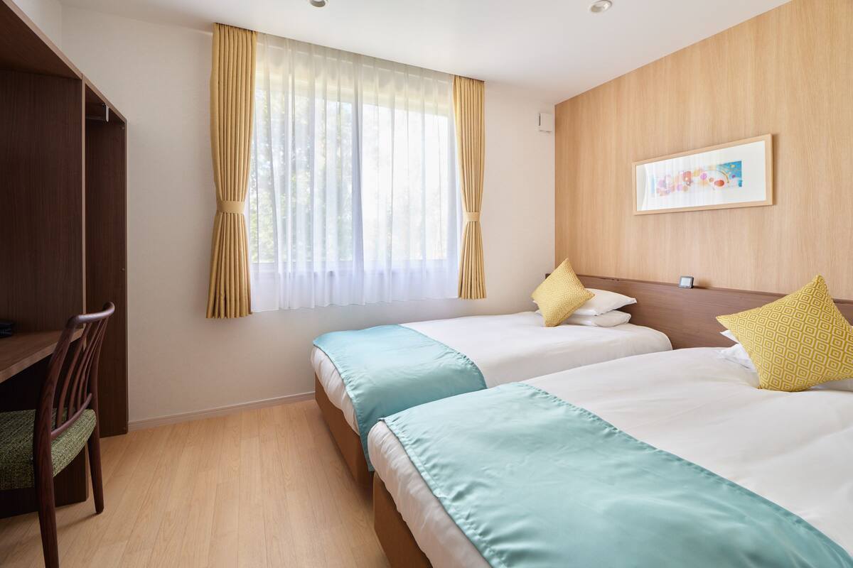 A hotel room with two beds, a desk, and a window with curtains.