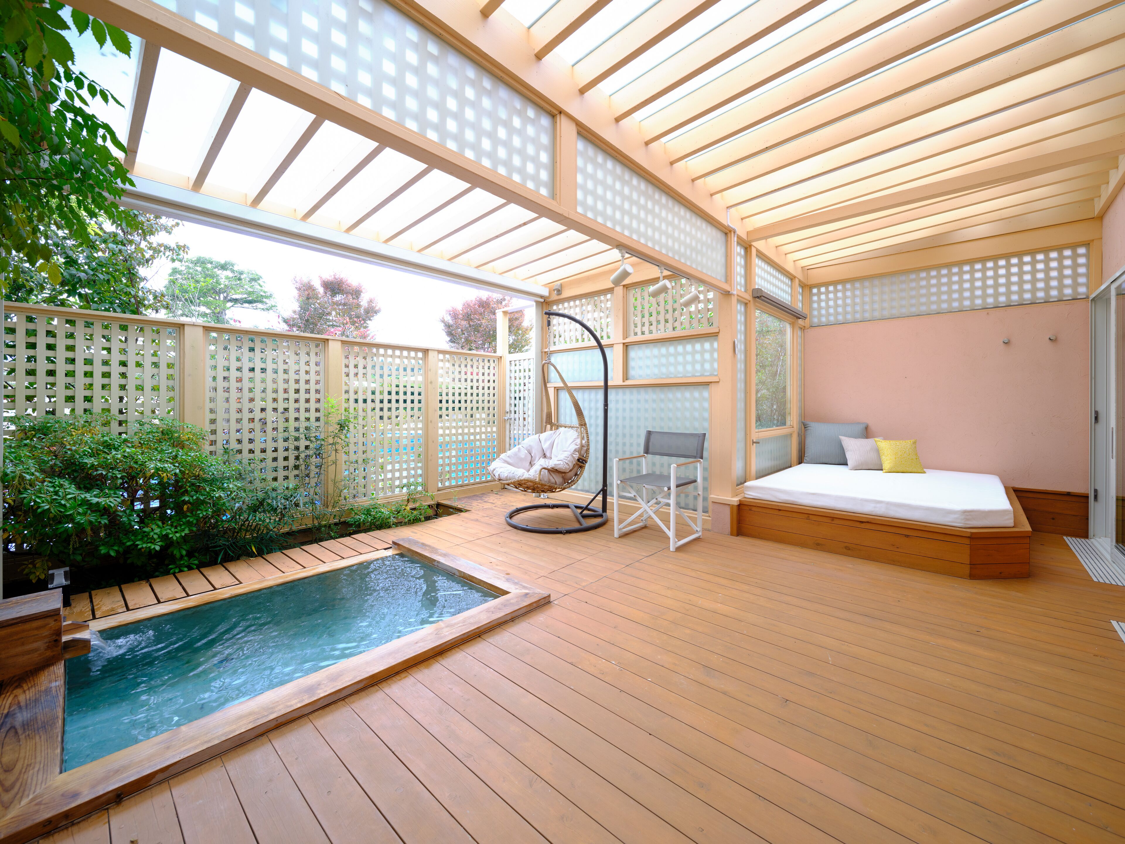 Un ambiente tipo spa con una terraza de madera, un jacuzzi, una zona de estar con una mecedora y una cama con almohadas.