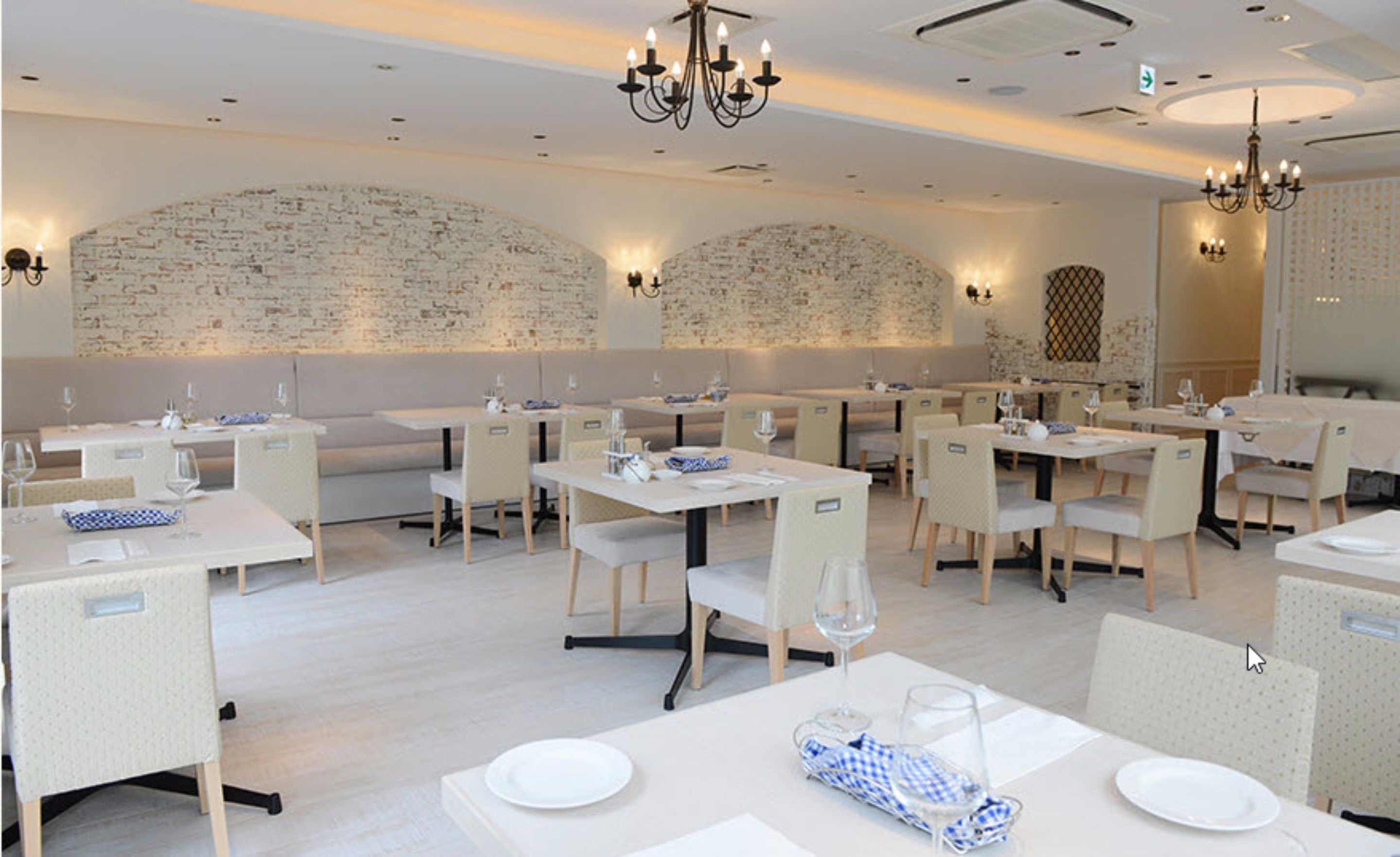 Ein Restaurant mit weißen Tischen und Stühlen, einer Ziegelwand und Kronleuchtern.