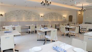 Ein Restaurant mit weißen Tischen und Stühlen, einer Ziegelwand und Kronleuchtern.