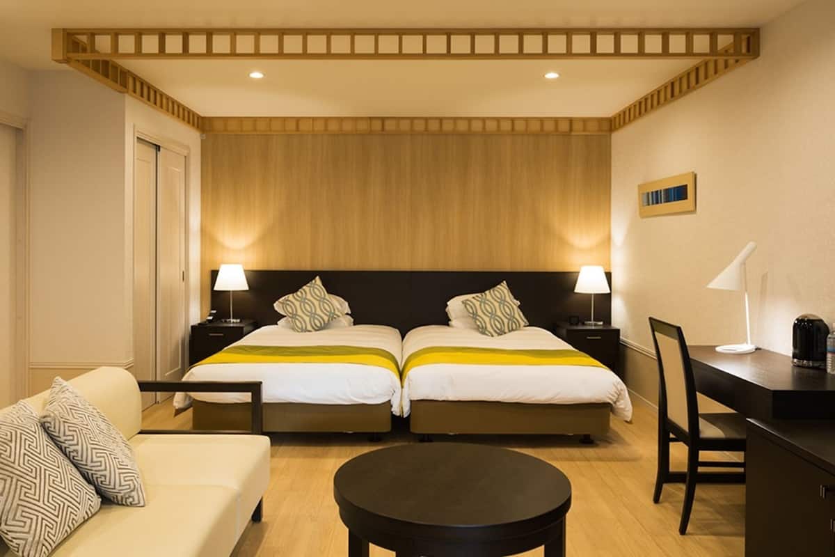 Ein Hotelzimmer mit zwei Betten, einer Schlafcouch, einem Schreibtisch und einem Sessel.