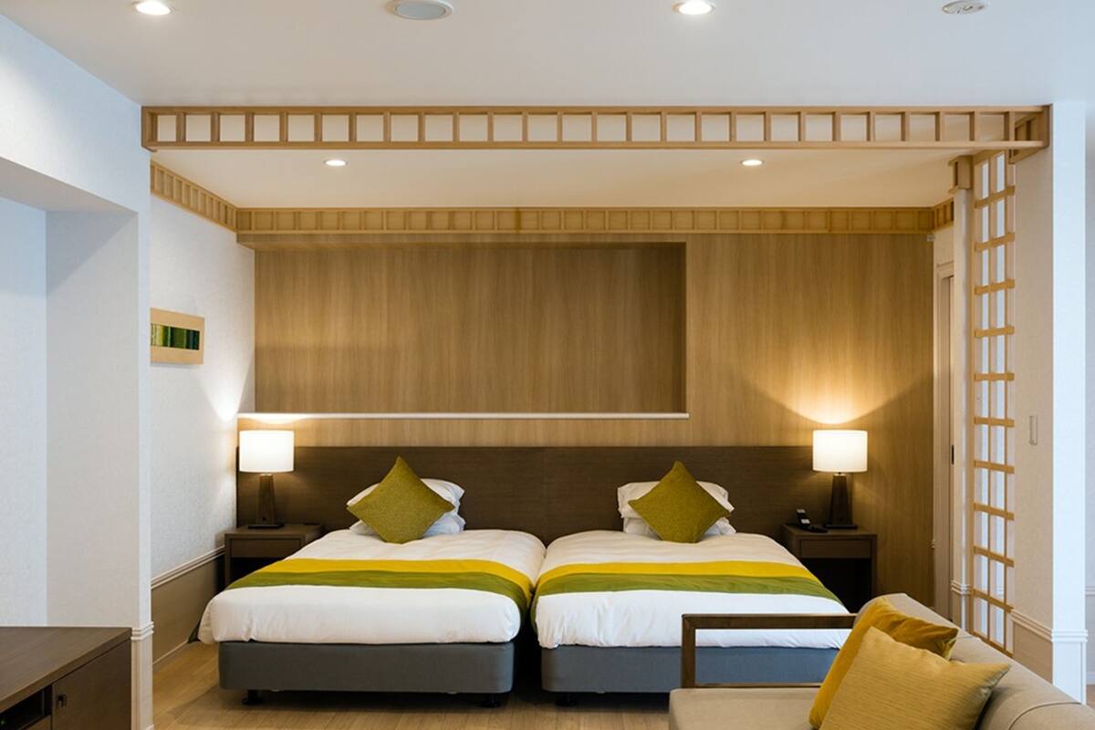 A hotel room with two beds, a sofa, a small table with a cup, and wooden paneling on the walls.