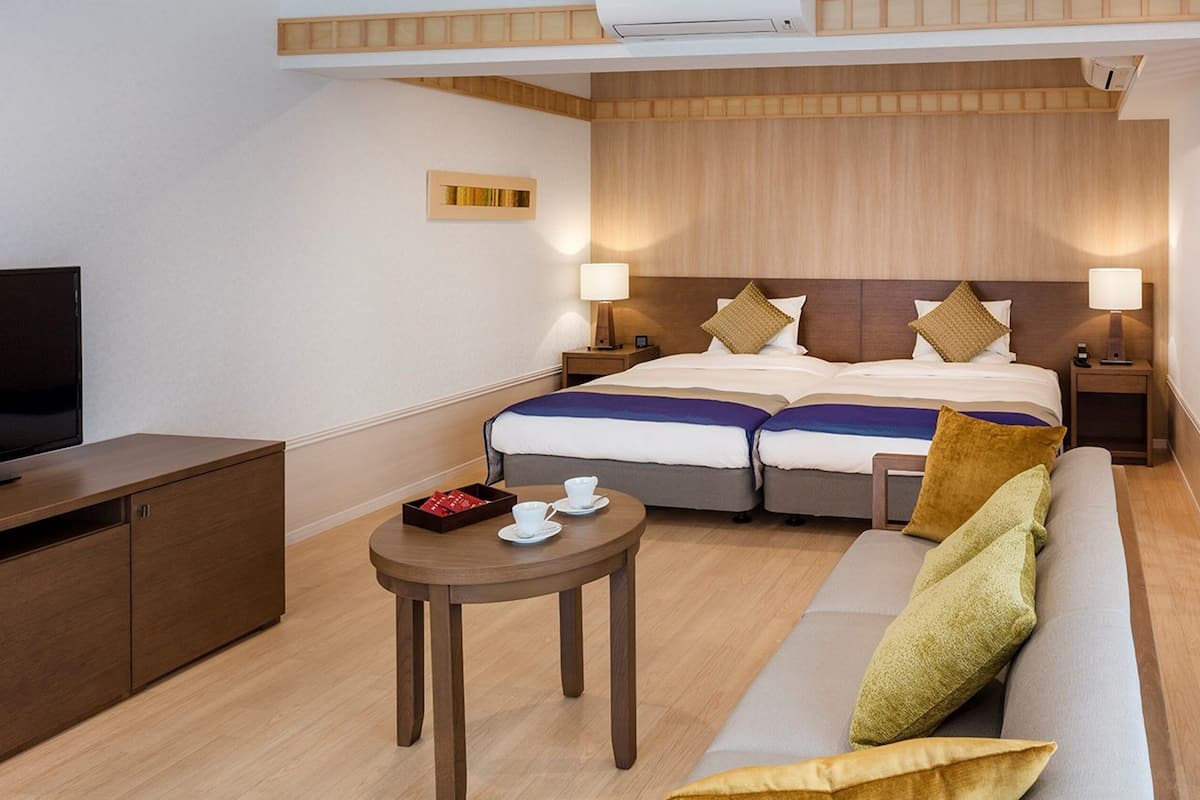 Ein Hotelzimmer mit einem Bett, zwei Nachttischen, einem Fernseher, einem Sofa und einem kleinen Tisch mit Tassen und einer Schachtel.
