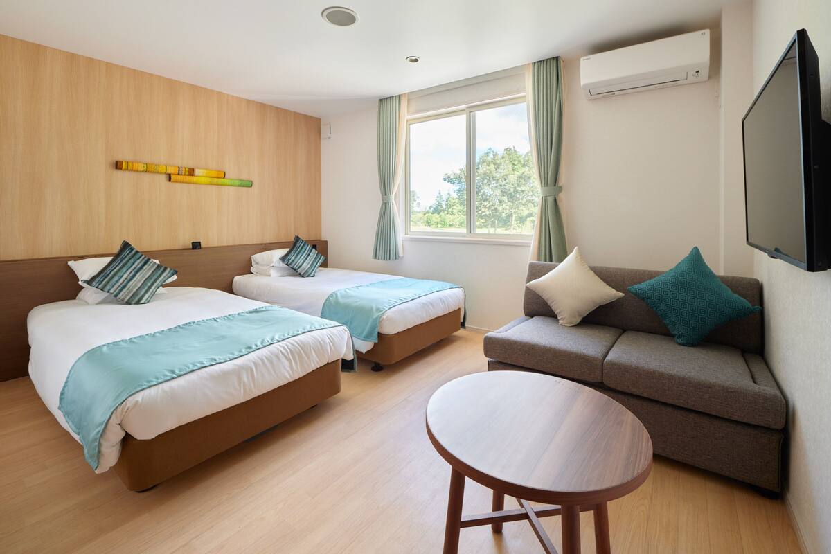 A hotel room with two beds, a sofa, a round table, and a TV.