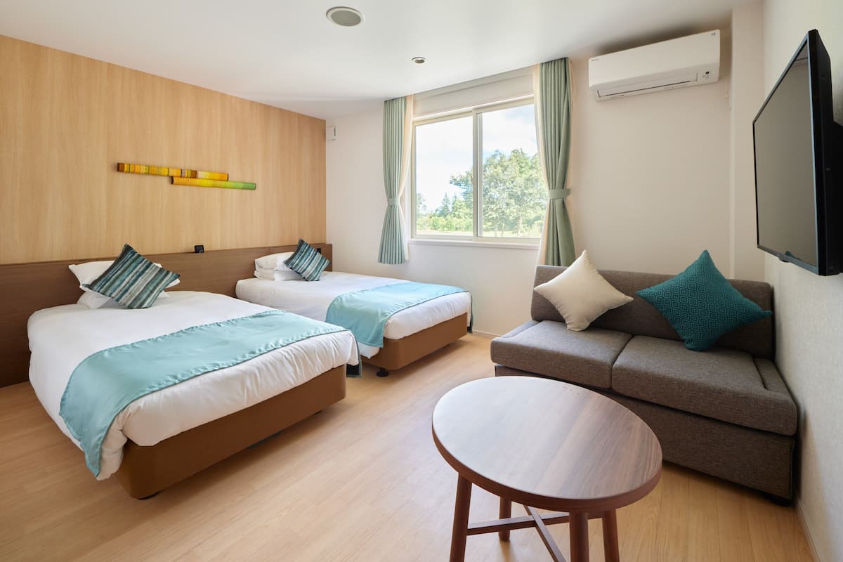 Ein Hotelzimmer mit zwei Betten, einem Schlafsofa, einem runden Tisch und einem Fernseher.