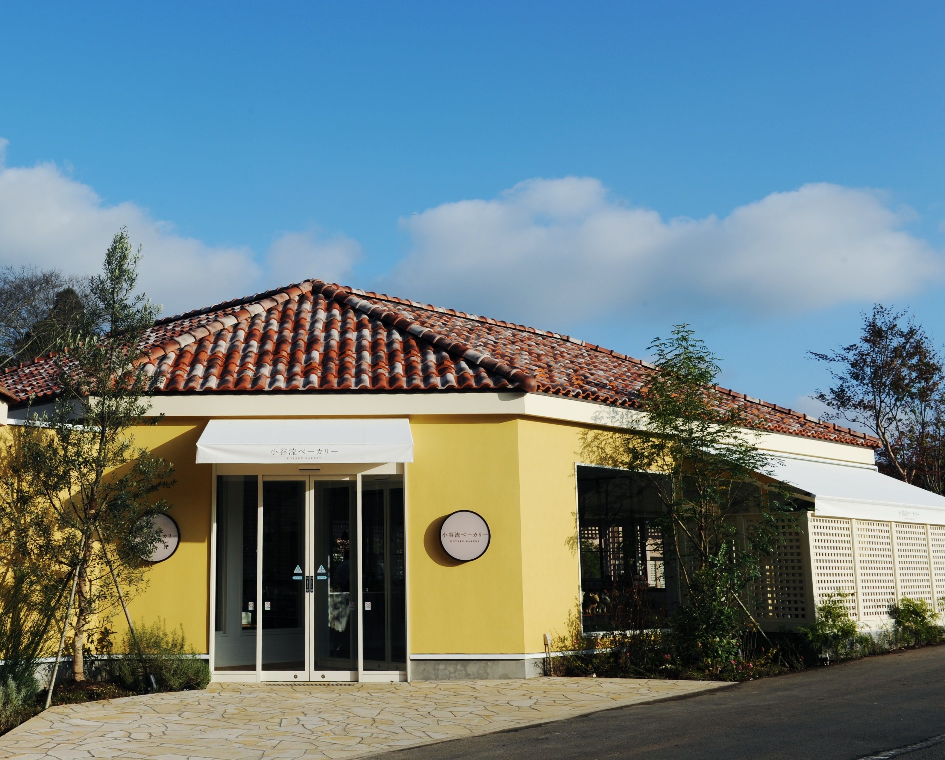 A yellow building with a tiled roof, a glass entrance, and a sign that reads "Hotel Bar".