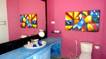 Un baño con una pared rosa, un lavabo azul y dos cuadros abstractos.