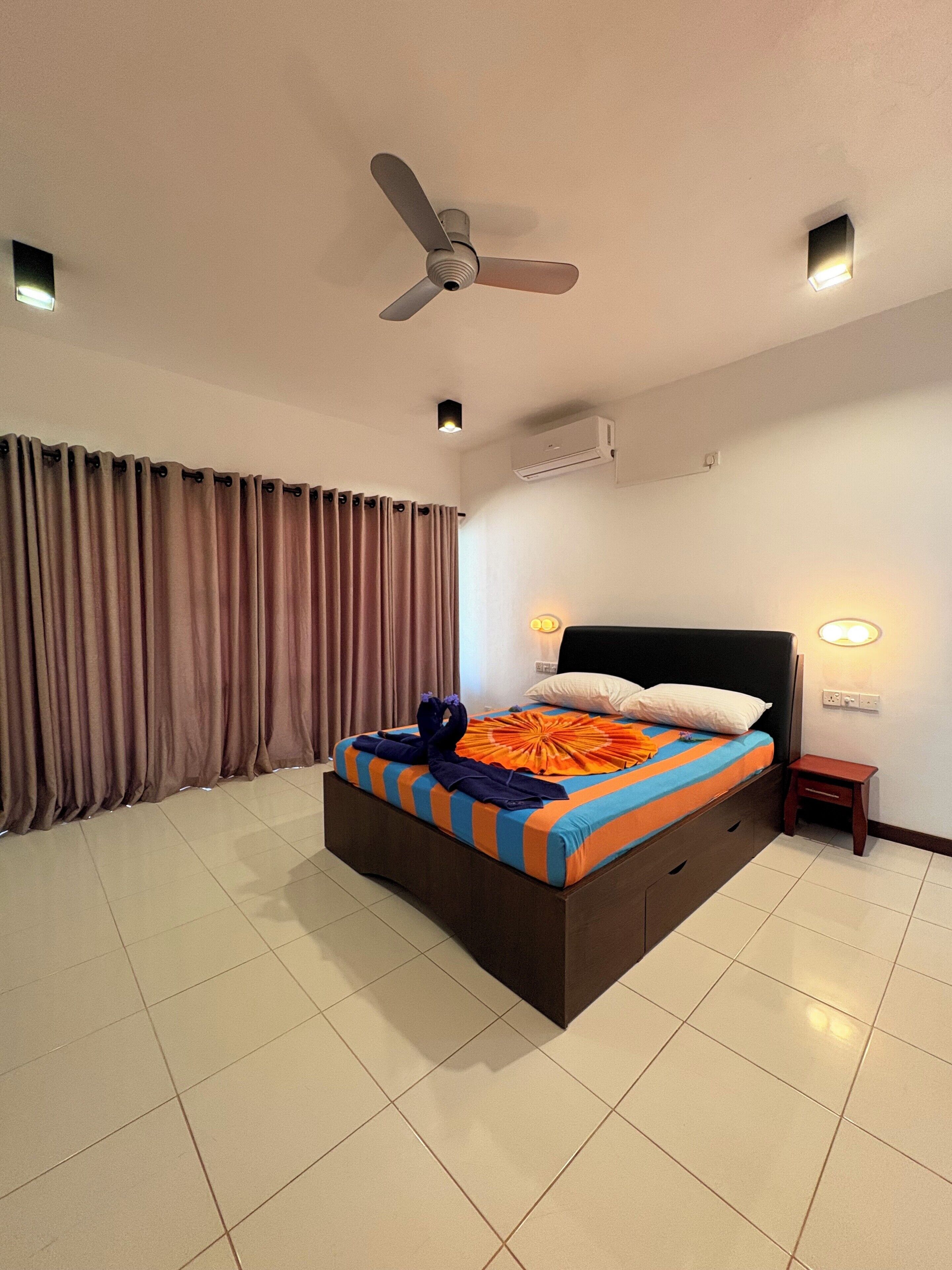 Habitación de hotel con cama, cortinas, ventilador de techo, aire acondicionado y lámparas de noche.