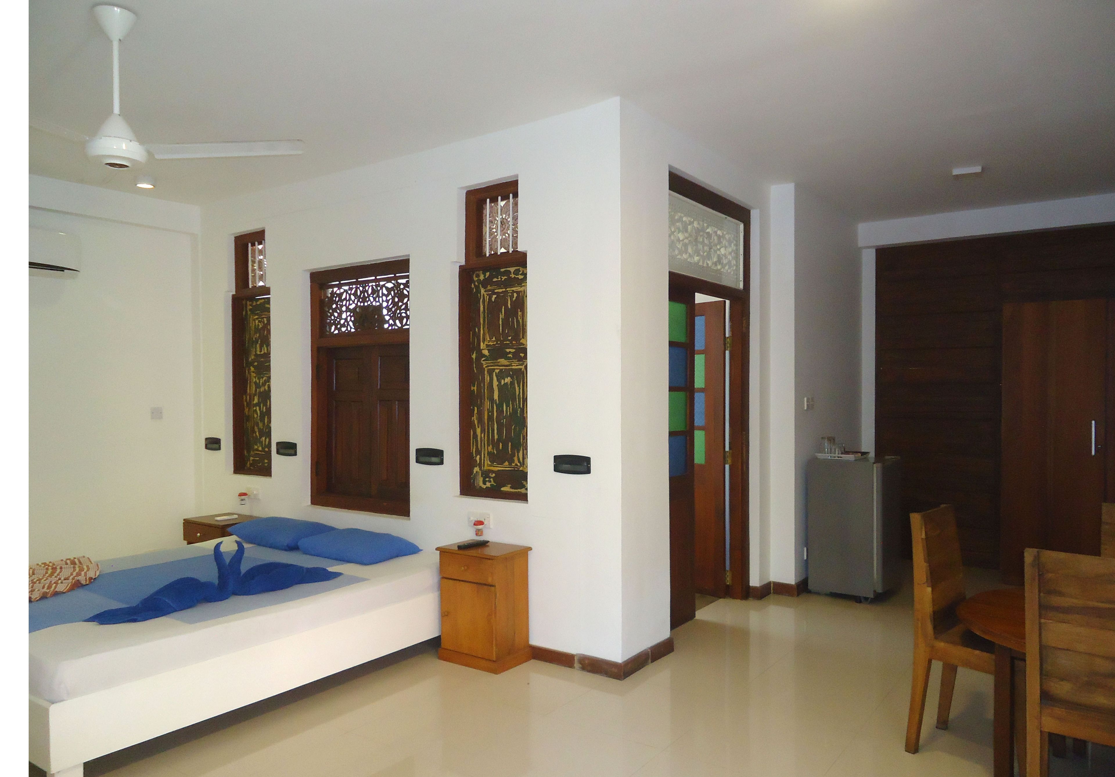 A hotel room with a bed, a small wooden nightstand, a ceiling fan, and a dining area with a table and chairs.