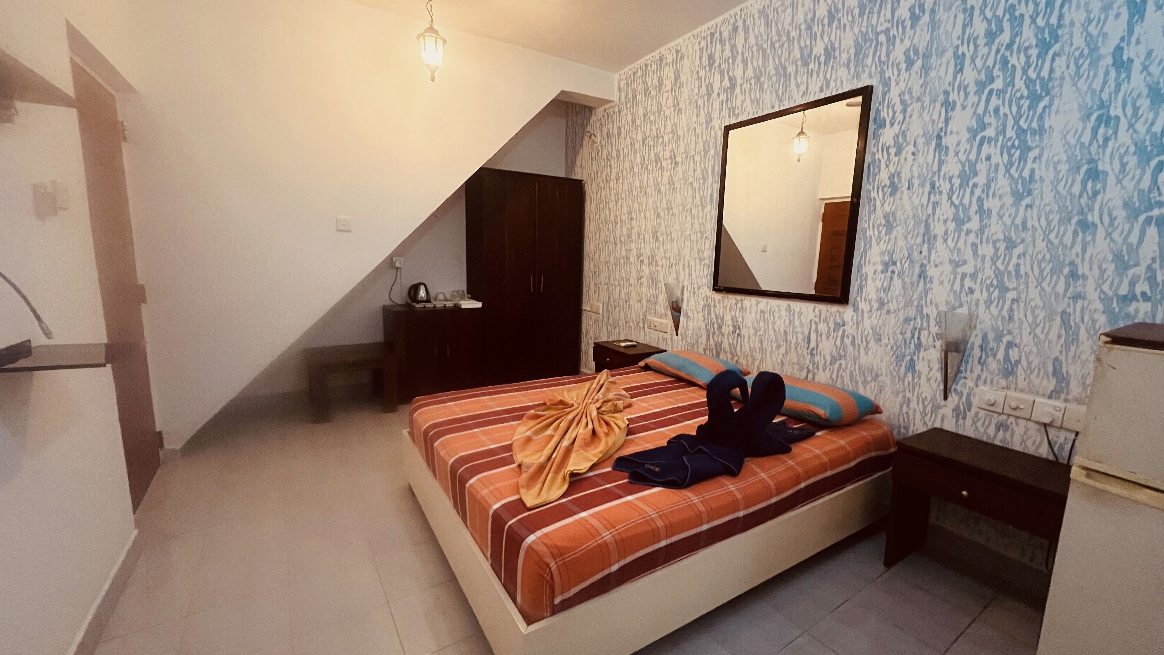 Ein Schlafzimmer mit Bett, Nachttisch, Kommode, Spiegel und einer Pendelleuchte.