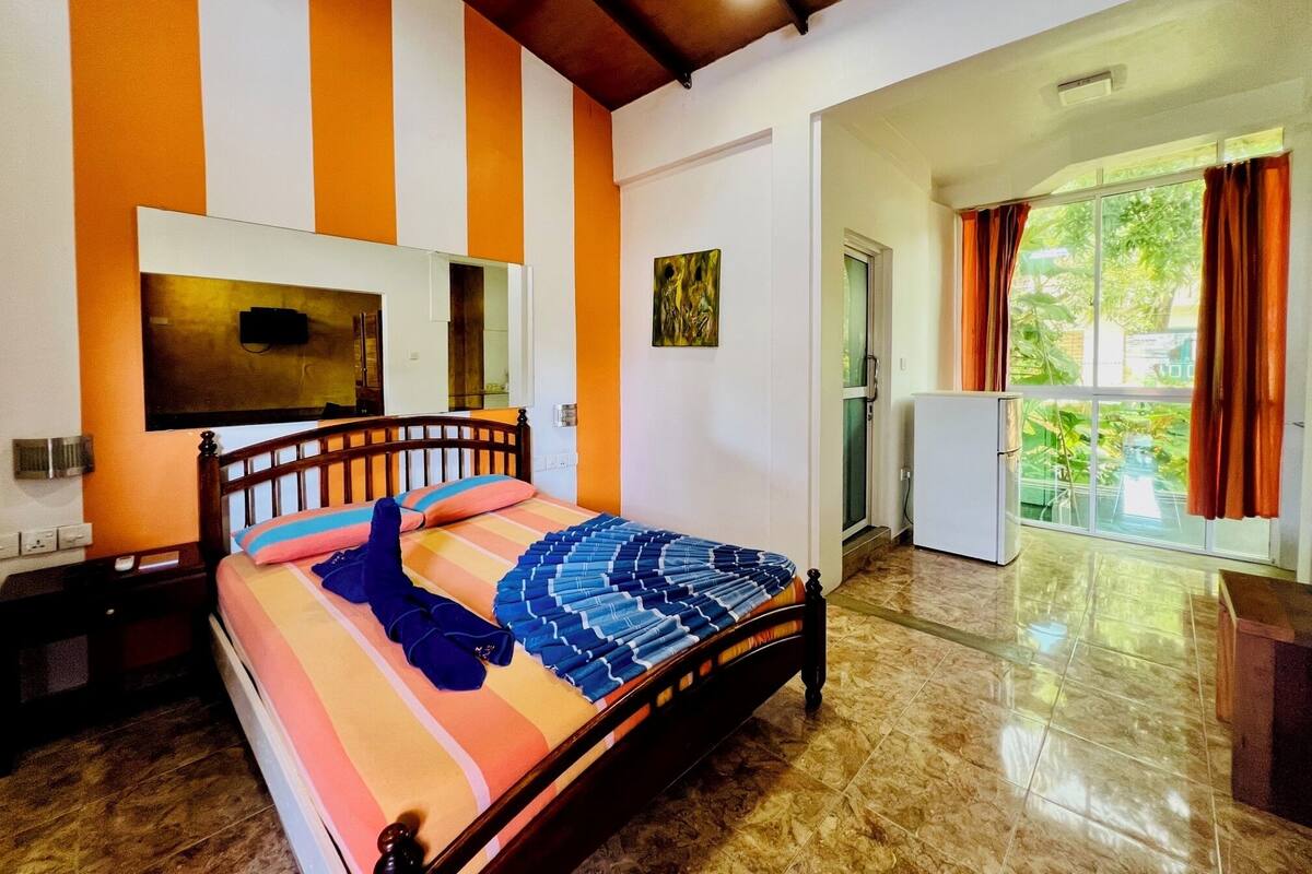 A bedroom with a bed, a TV, a door, and a window.