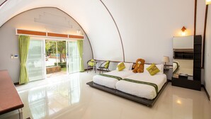 Une chambre d’hôtel spacieuse et moderne, dotée d’un plafond incurvé, d’un grand lit avec une literie blanche et des touches de vert, d’une table de chevet, d’une chaise et d’une vue sur l’extérieur grâce à une porte vitrée.