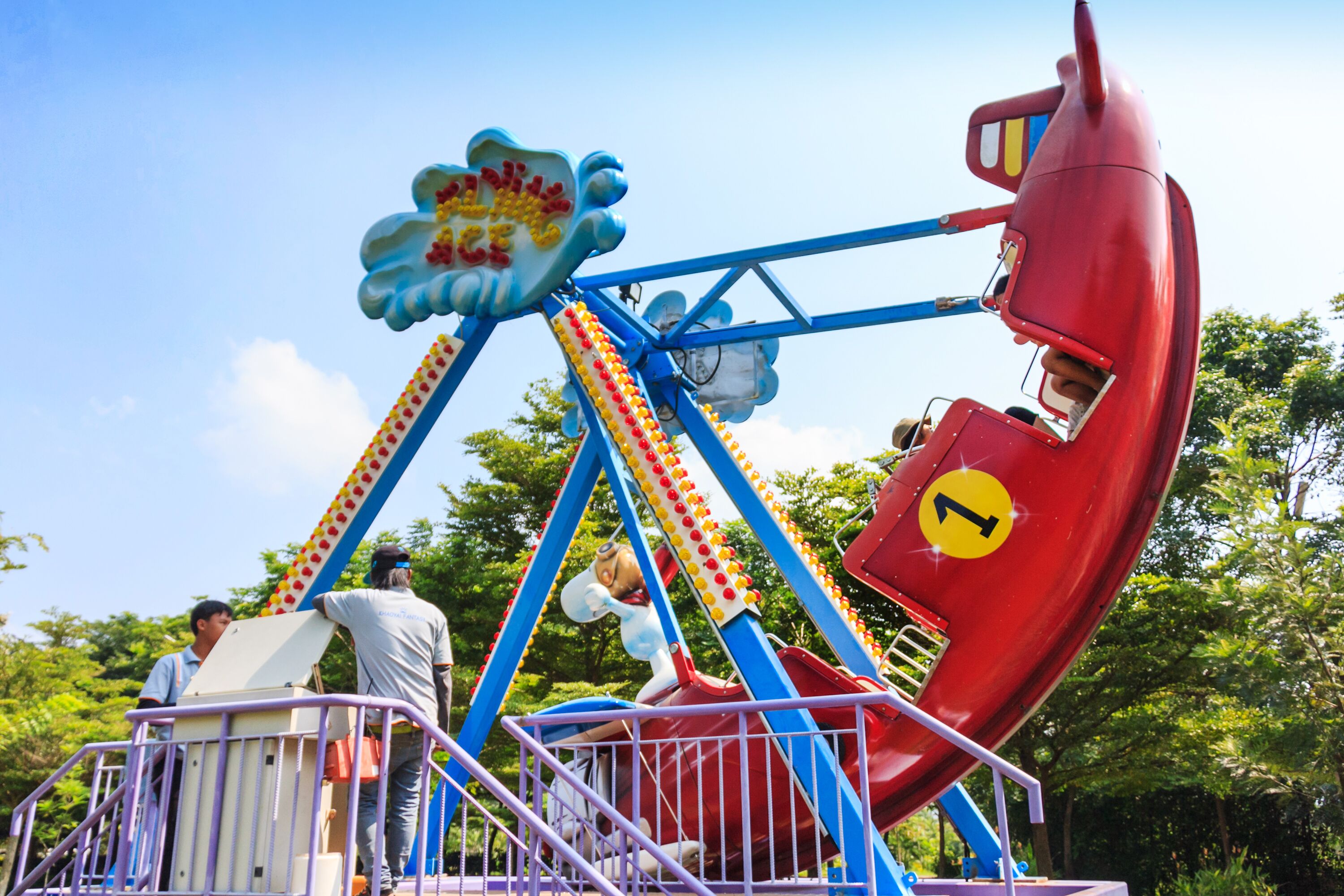 A swing ride with a red seat and a blue frame, surrounded by greenery.