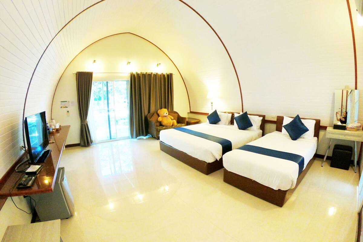 Habitación de hotel con dos camas, un escritorio con computadora, televisión y un amplio ventanal de arco.